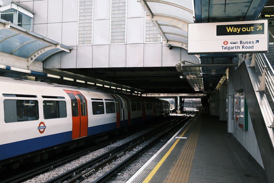 A view of Hayes and Harlington station platform during daytime showing a partially visible London Underground train with white, red, and blue exterior parked alongside the platform. The platform has a