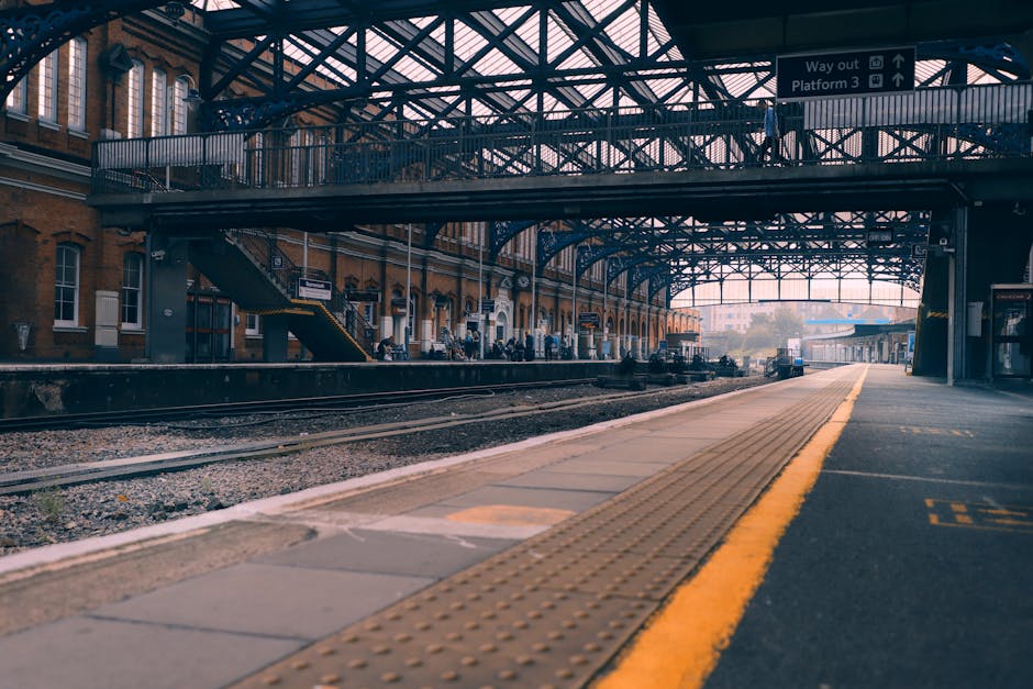A view of Hayes and Harlington station platform during daytime showing a partially visible London Underground train with white, red, and blue exterior parked alongside the platform. The platform has a